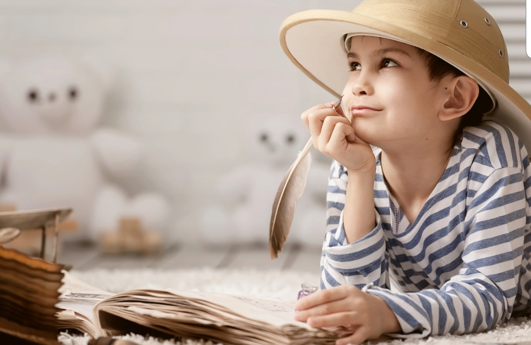 Un enfant rêve devant un livre avec une plume, comme s'il avait du mal à écrire